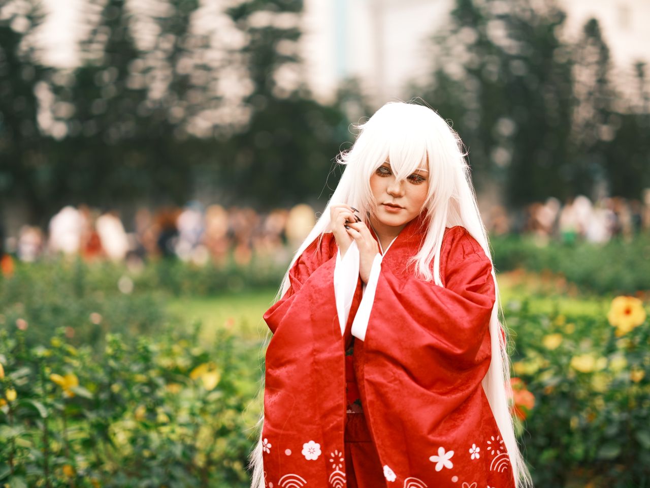 elegant cosplayer in traditional red attire posing outdoors in a lush