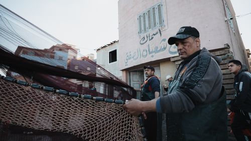 Free A group of fishermen manage nets near a building, showcasing daily life and teamwork. Stock Photo