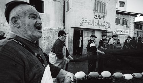 Free Black and white photo of a group of fishermen collaborating on a street in an urban setting. Stock Photo