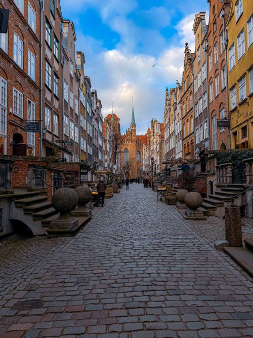 Free Beautiful cobblestone street in Gdańsk lined with historic buildings leading to St. Mary's Church. Stock Photo