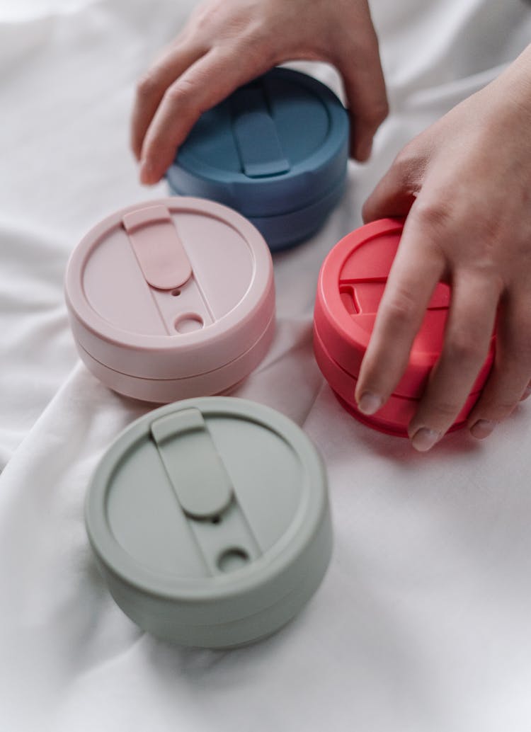 Person Holding  Plastic Round Containers On White Textile