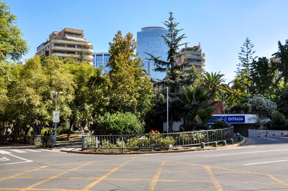Escena soleada de una calle urbana con exuberante vegetación y rascacielos de Santiago.