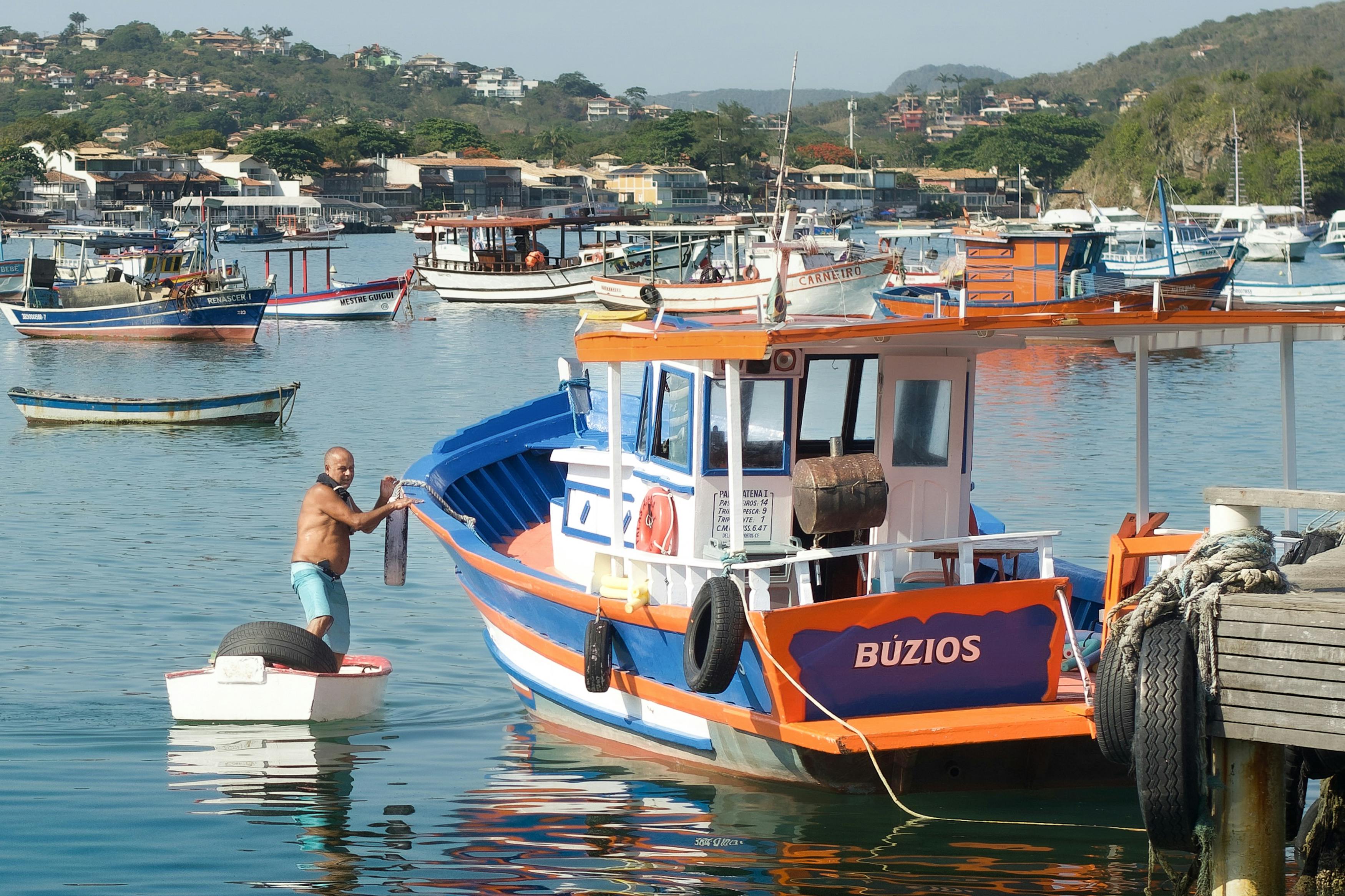 Scenic view of colorful fishing boats docked at Búzios, Brazil. A man on a small boat adds charm to the vibrant marina.
