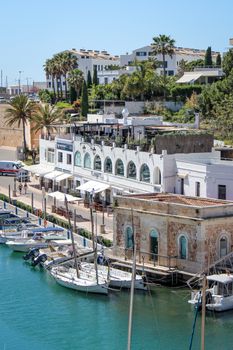 Charming harbor scene in Ciutadella, Spain, with boats and white buildings under a bright sky.