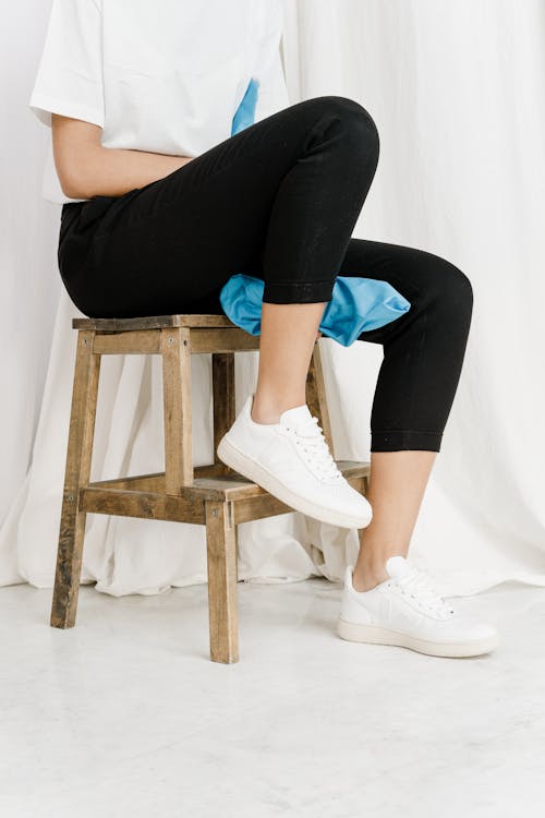 Person in Black Leggings and White Sneakers Sitting on Brown Wooden Stool