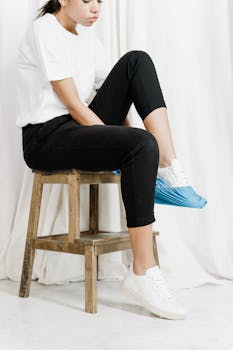 Woman wearing black pants and white sneakers sits on a stool indoors, showcasing a casual style.