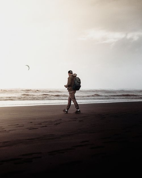 Free A man enjoying a serene walk along a New Zealand beach at dawn with a backpack and a sweeping view of the ocean. Stock Photo