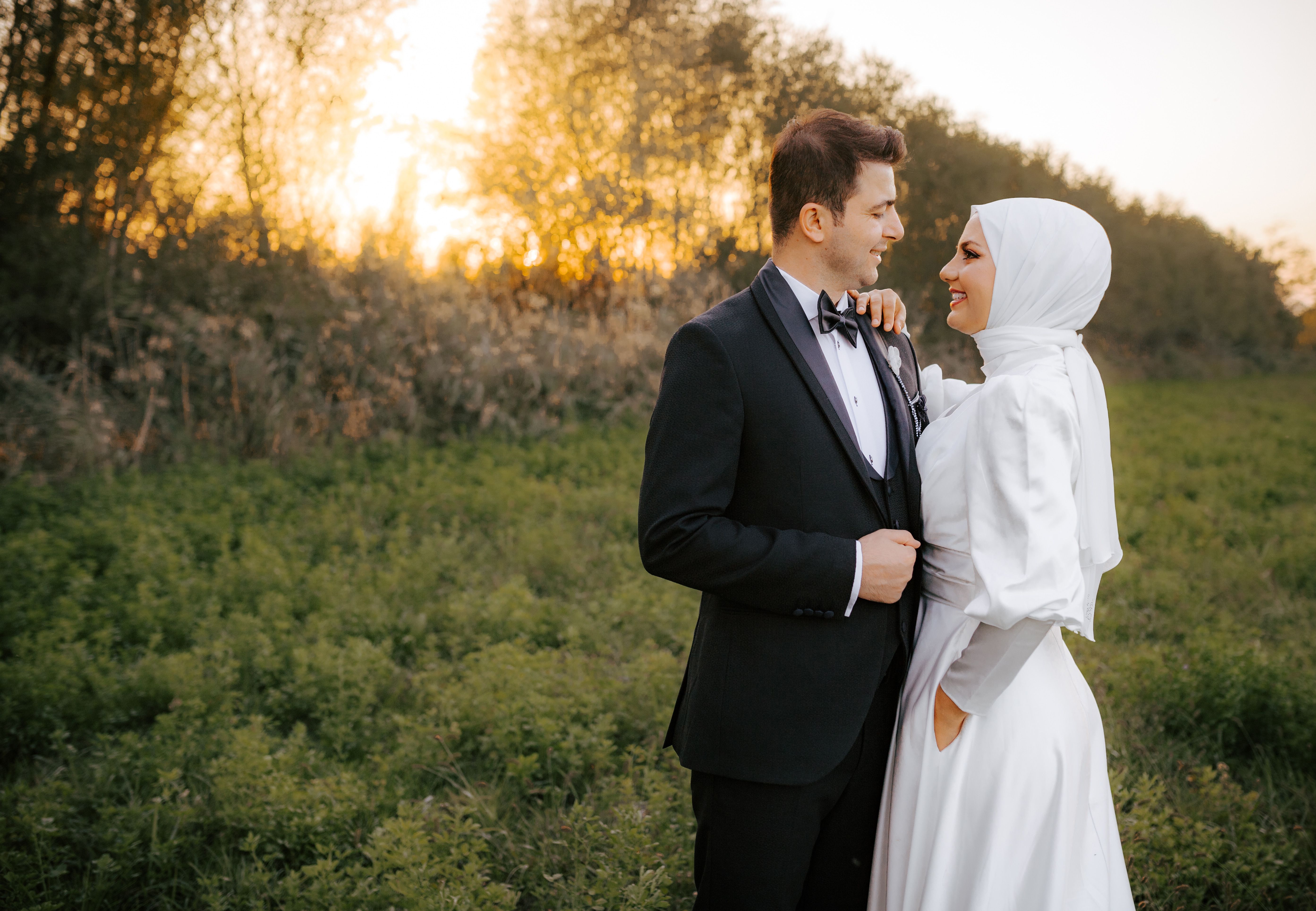 Elegant bride and groom embracing at sunset in a lush outdoor setting.