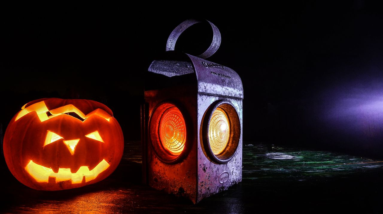 Glowing carved jack-o'-lantern beside a vintage metal lantern lit from within at night