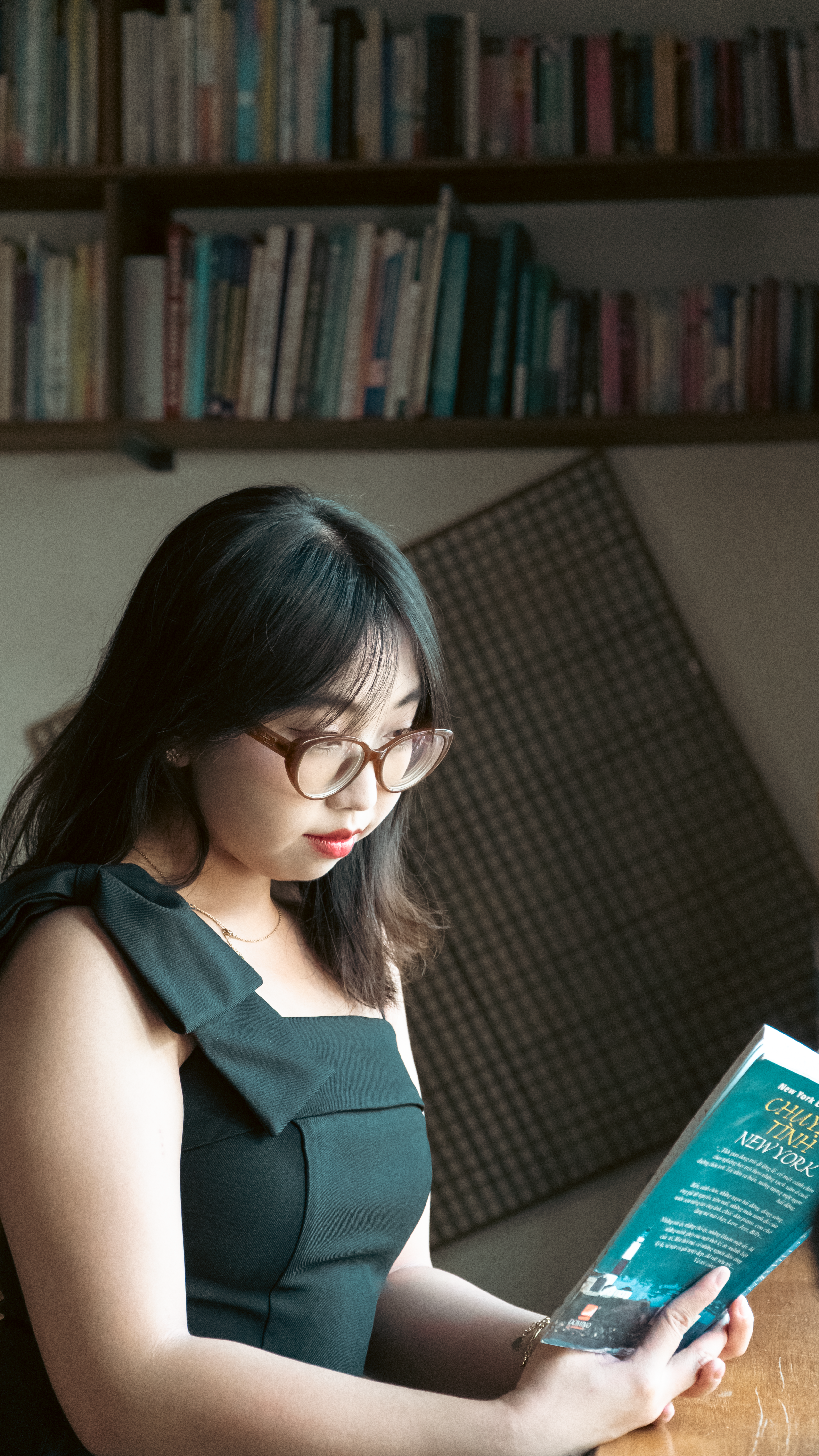 Young woman in glasses reading a book in a cozy indoor library setting.