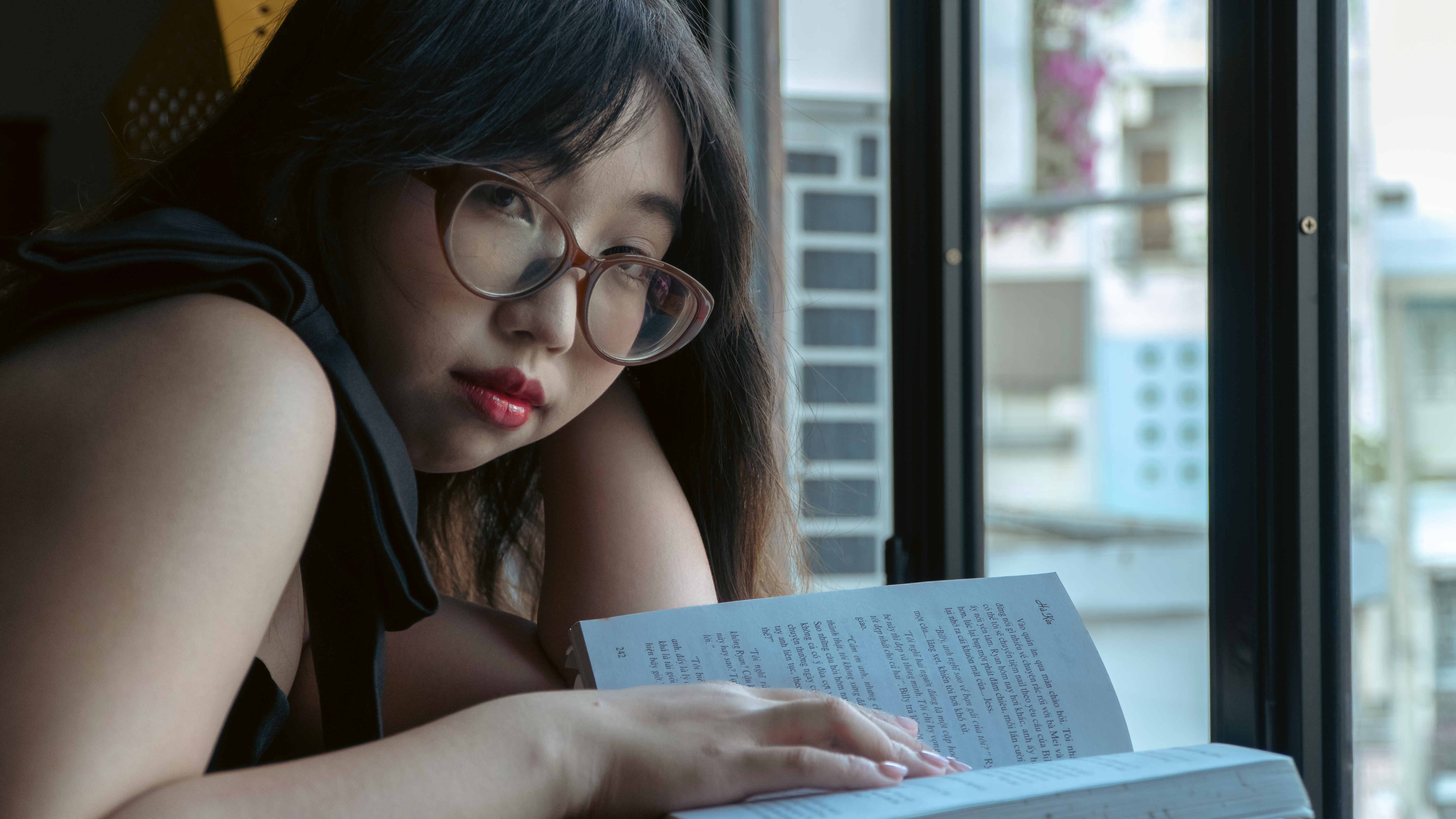Jovem estudando de maneira concentrada enquanto lê um livro próximo a uma janela, transmitindo foco e reflexão.