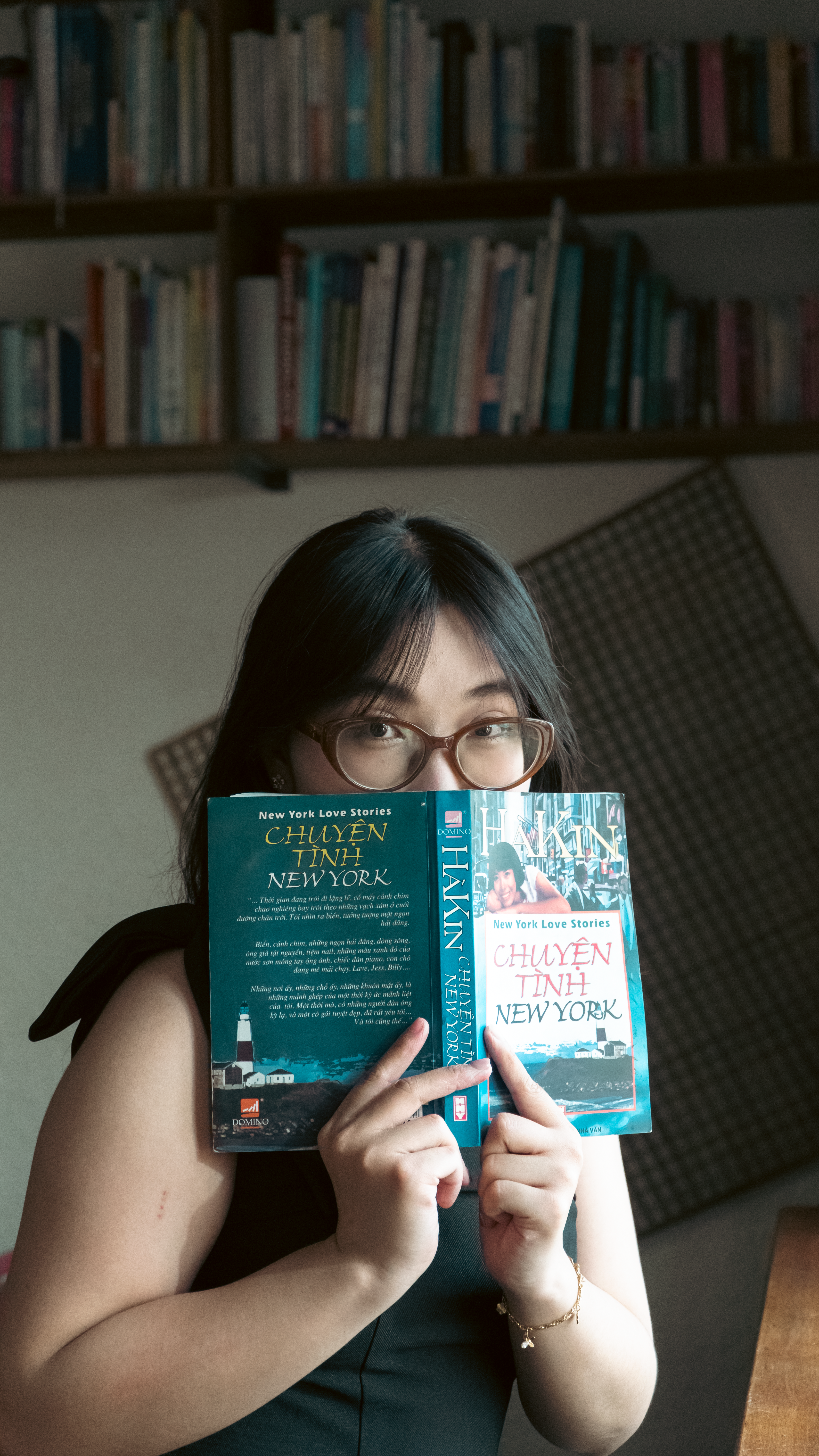 Young woman reading a New York themed book indoors by a bookshelf.