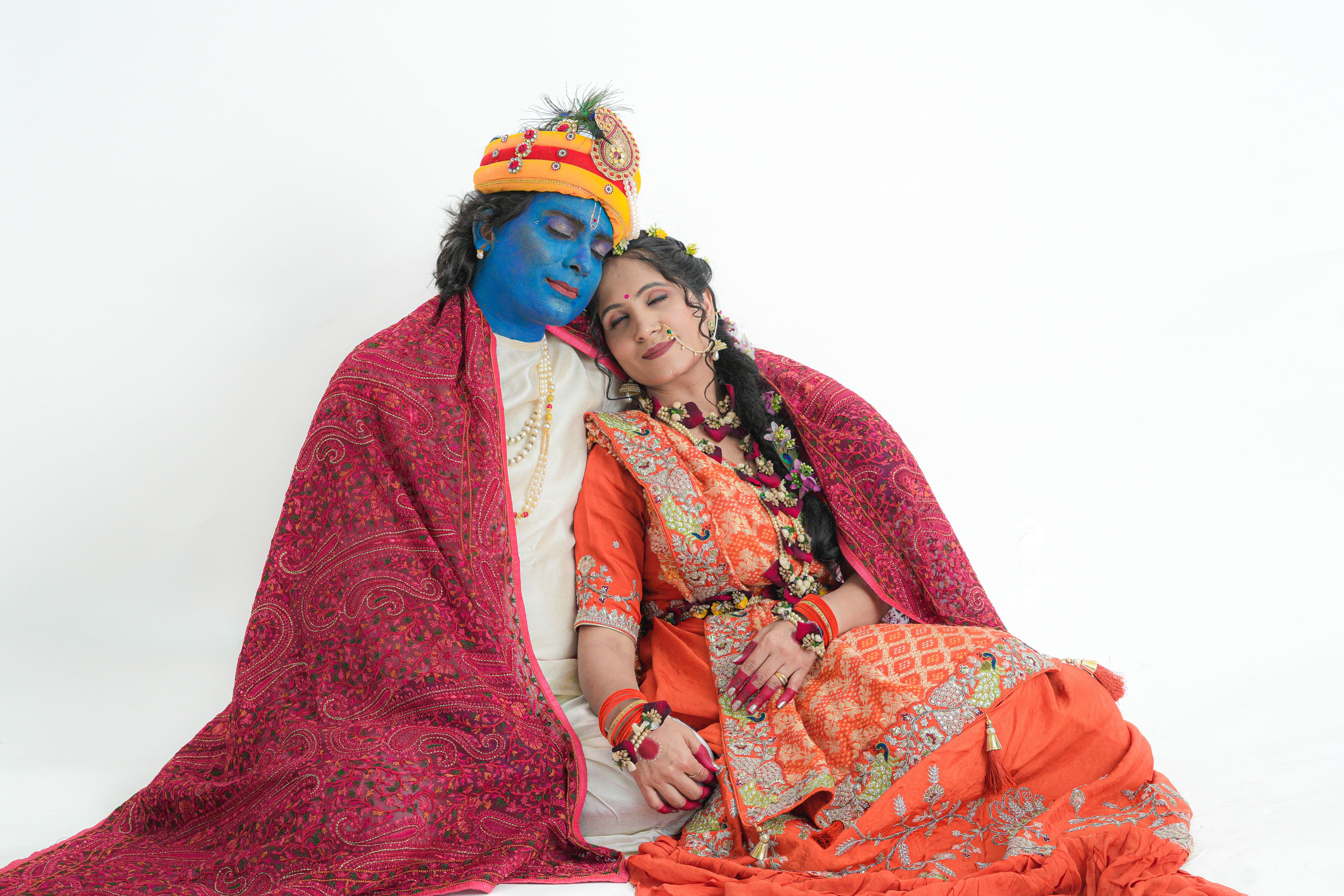 A couple dressed as traditional Indian deities with blue face paint in a colorful costume on a white background.