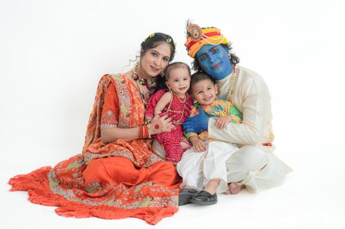 Free A family of four dressed in traditional attire with one member as Lord Krishna, smiling together against a white background. Stock Photo