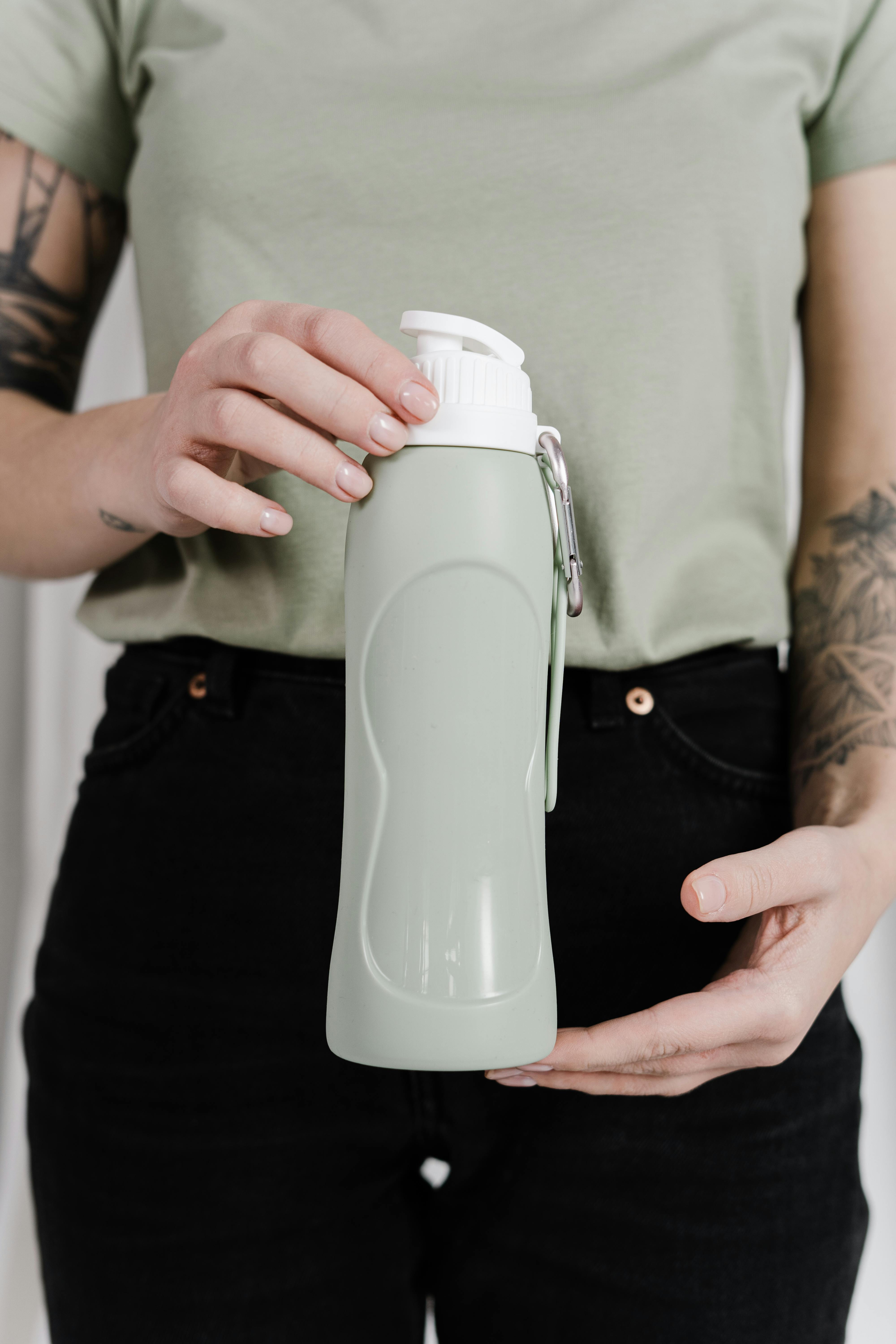 Person holding a reusable water bottle, promoting a zero-waste lifestyle and sustainability.