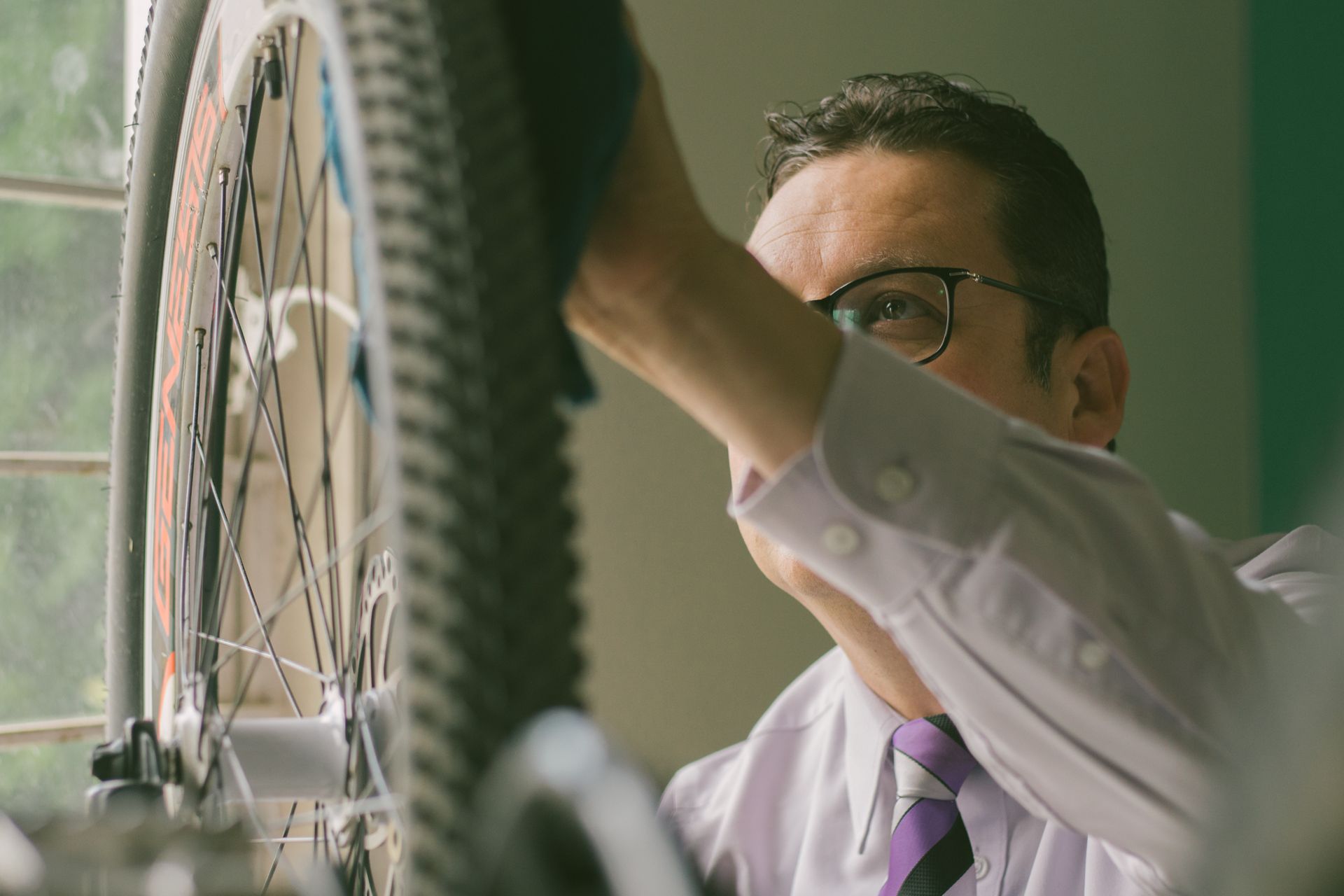 Adult man in a white shirt repairing a bicycle wheel indoors, using a cloth.