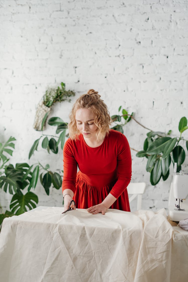 Woman Wearing Red Dress While Cutting White Cloth