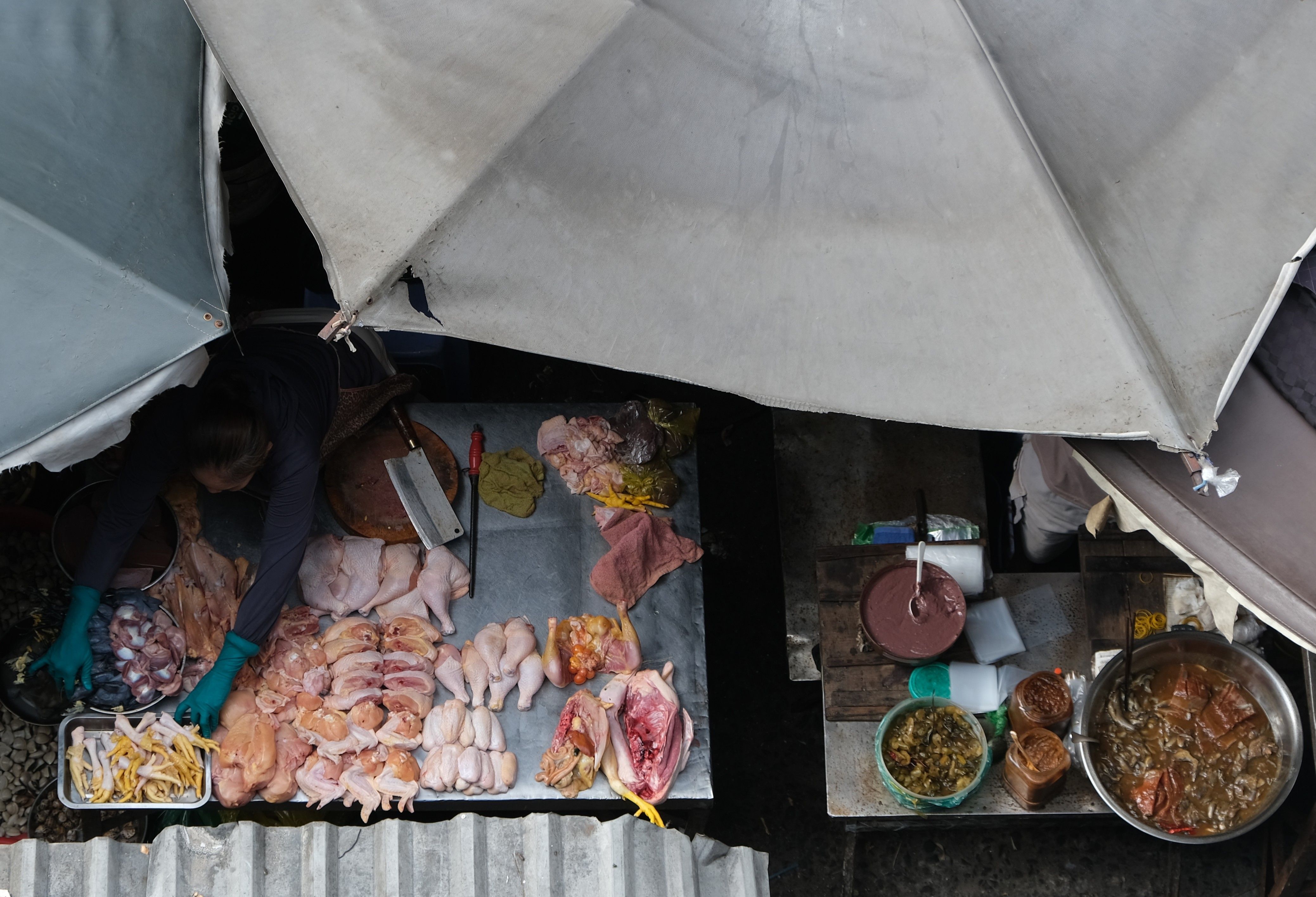Overhead view of a market stall selling various cuts of raw chicken under umbrellas.