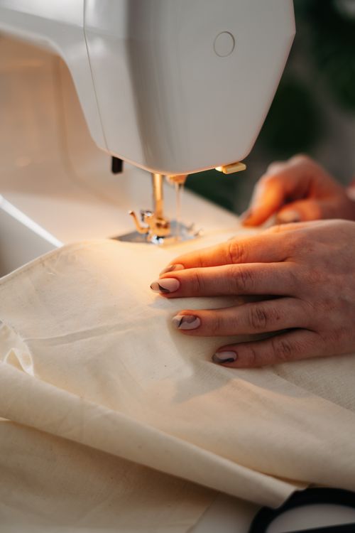 Primo piano editoriale di mani che guidano un tessuto chiaro durante una cucitura domestica