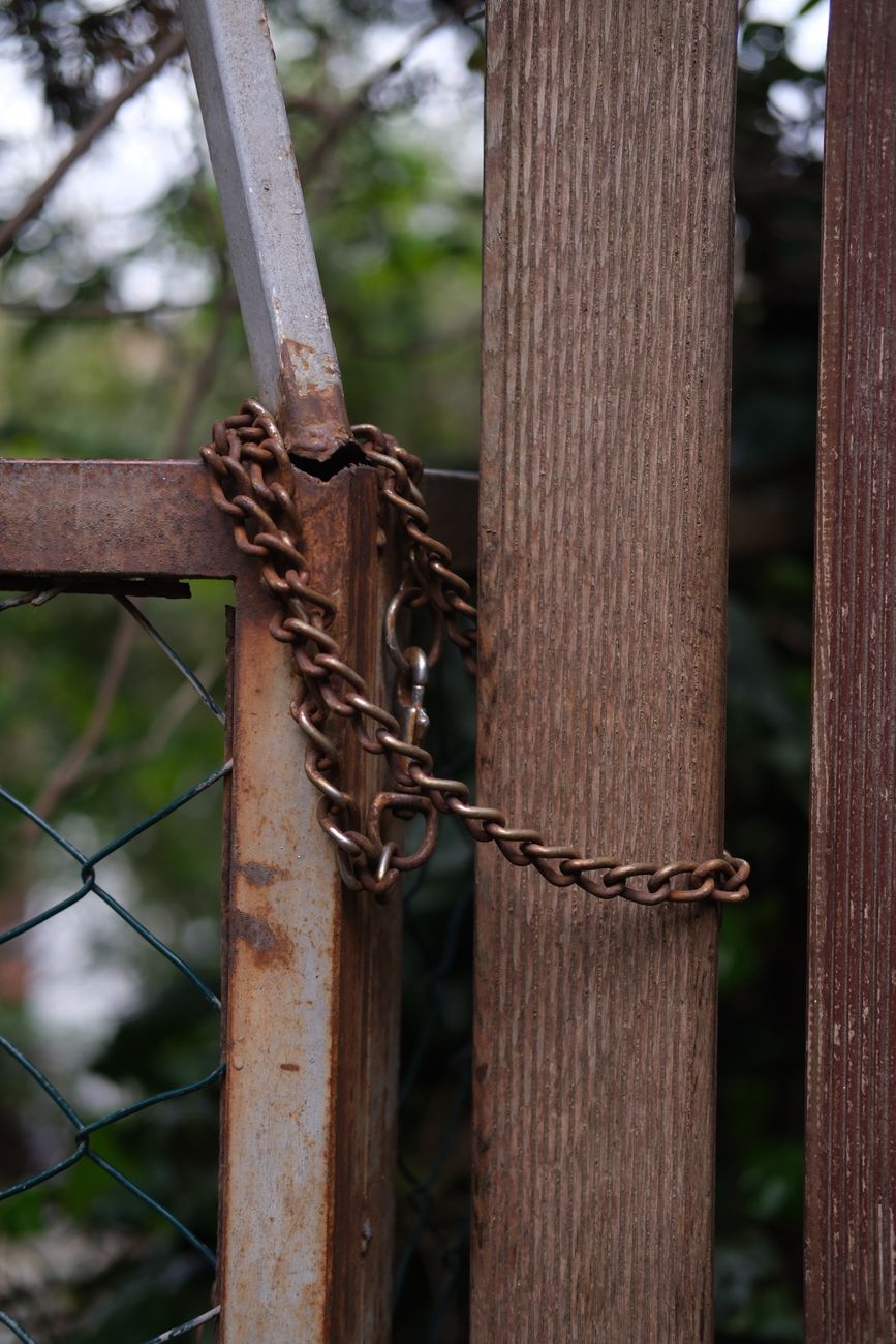 Close-up of a rusty chain wrapped around a weathered wooden and metal fence.