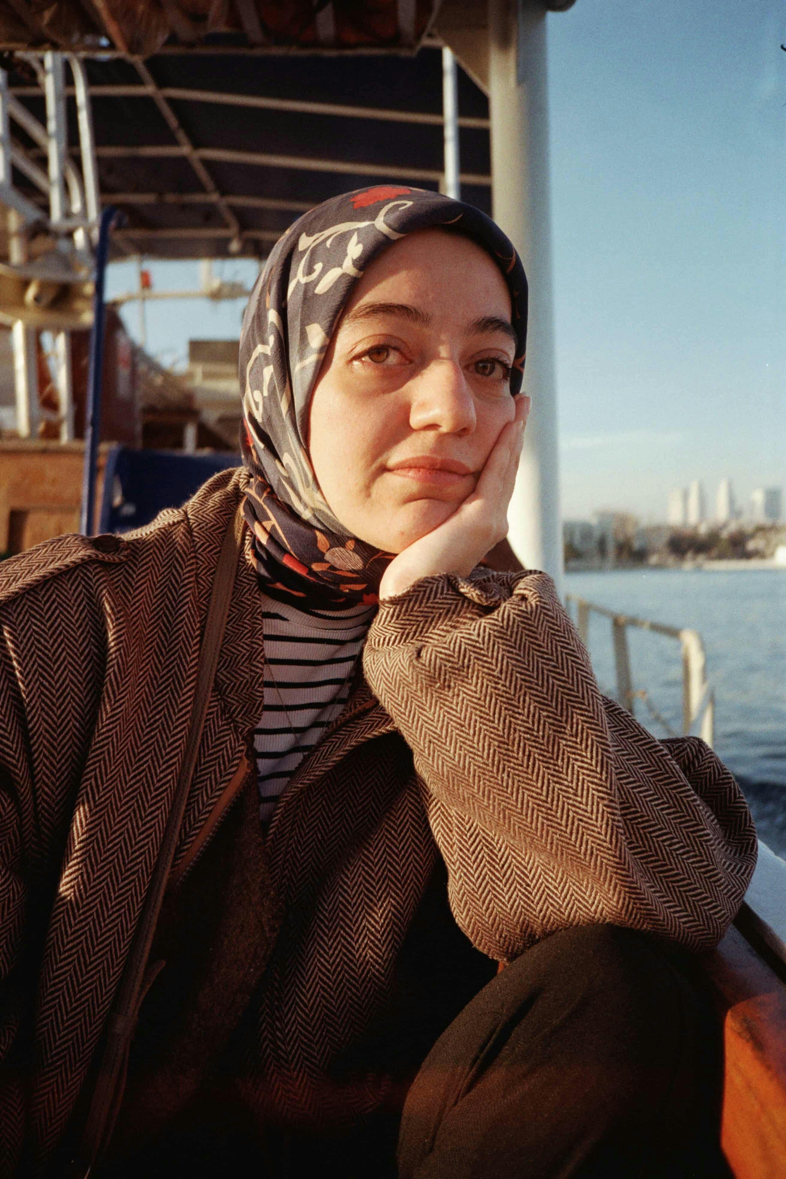 Woman on a boat reflecting by the water on a sunny day wearing a hijab.