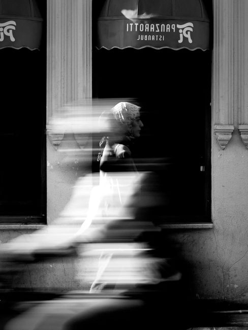 Black and white image capturing the motion blur of pedestrians in front of a cafe with Istanbul signage.