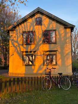 A picturesque yellow house with tree shadows and a bike against a fence in Linköping, Sweden.