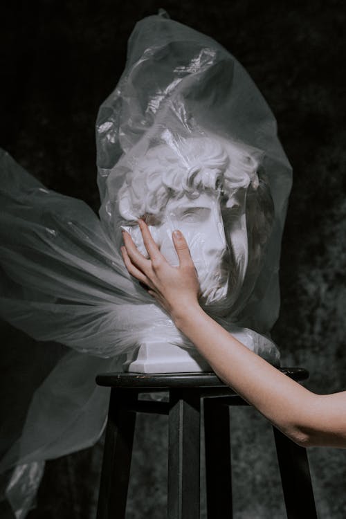 Person Holding Gypsum Head Covered With Plastic Bag