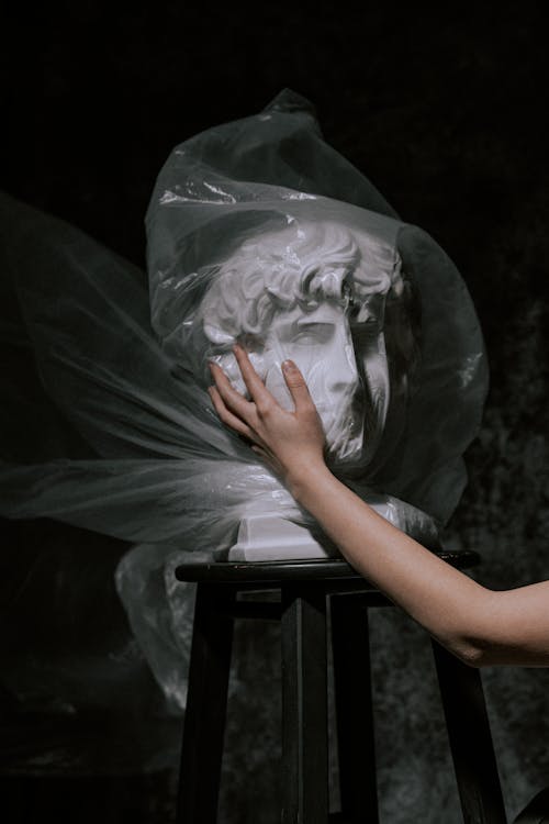 Person Holding Gypsum Head Covered With White Plastic Bag