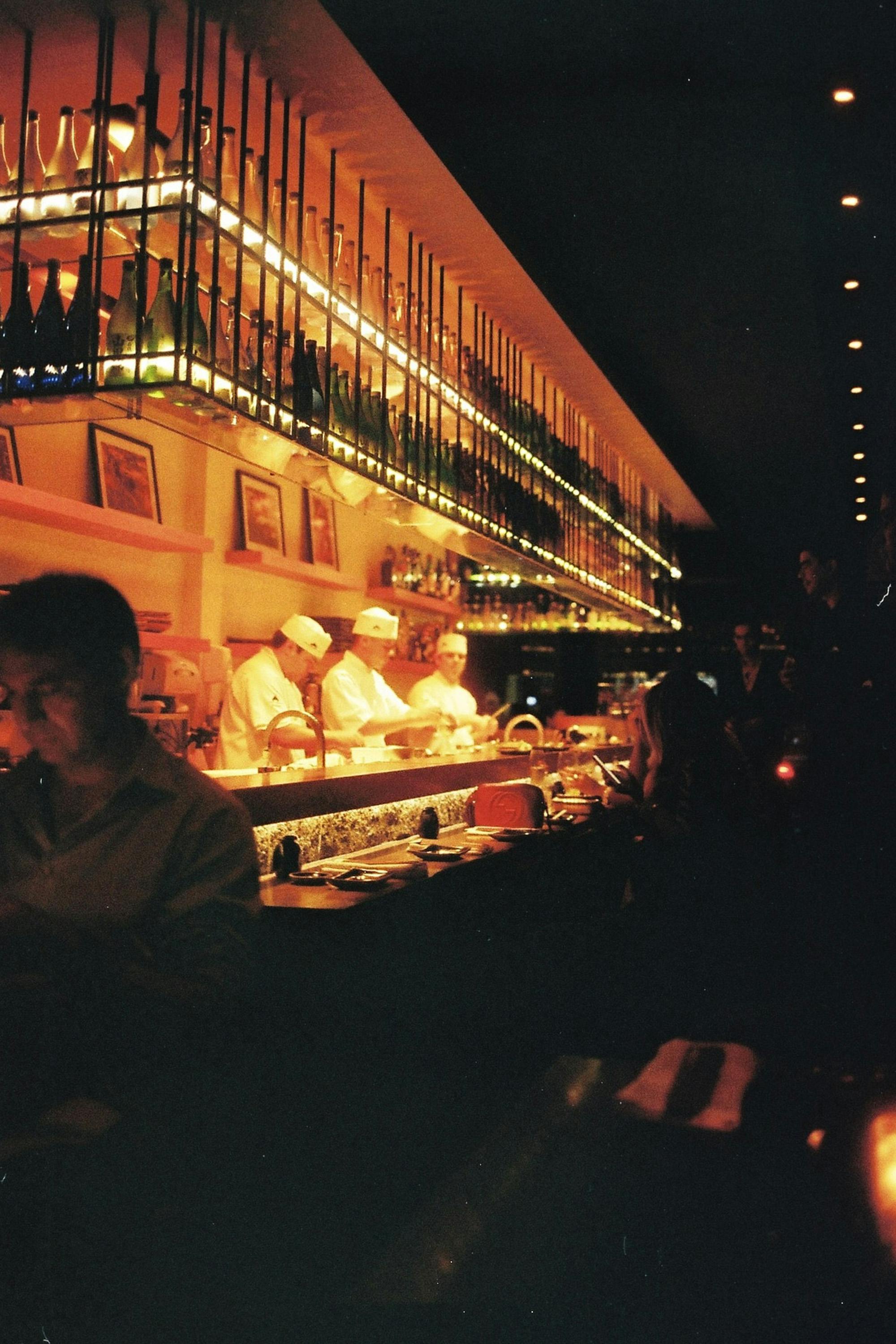 Chefs cooking in restaurant near male customer at night