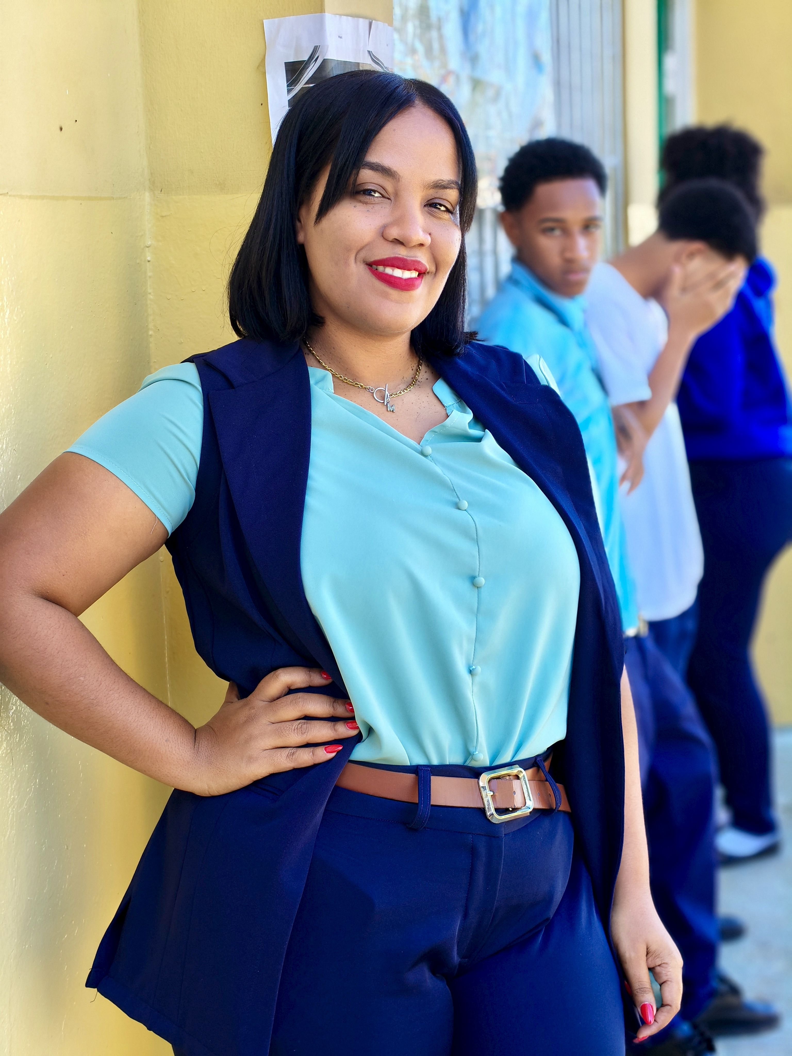 Confident woman in casual business attire smiling outdoors with three people in the background against a wall.
