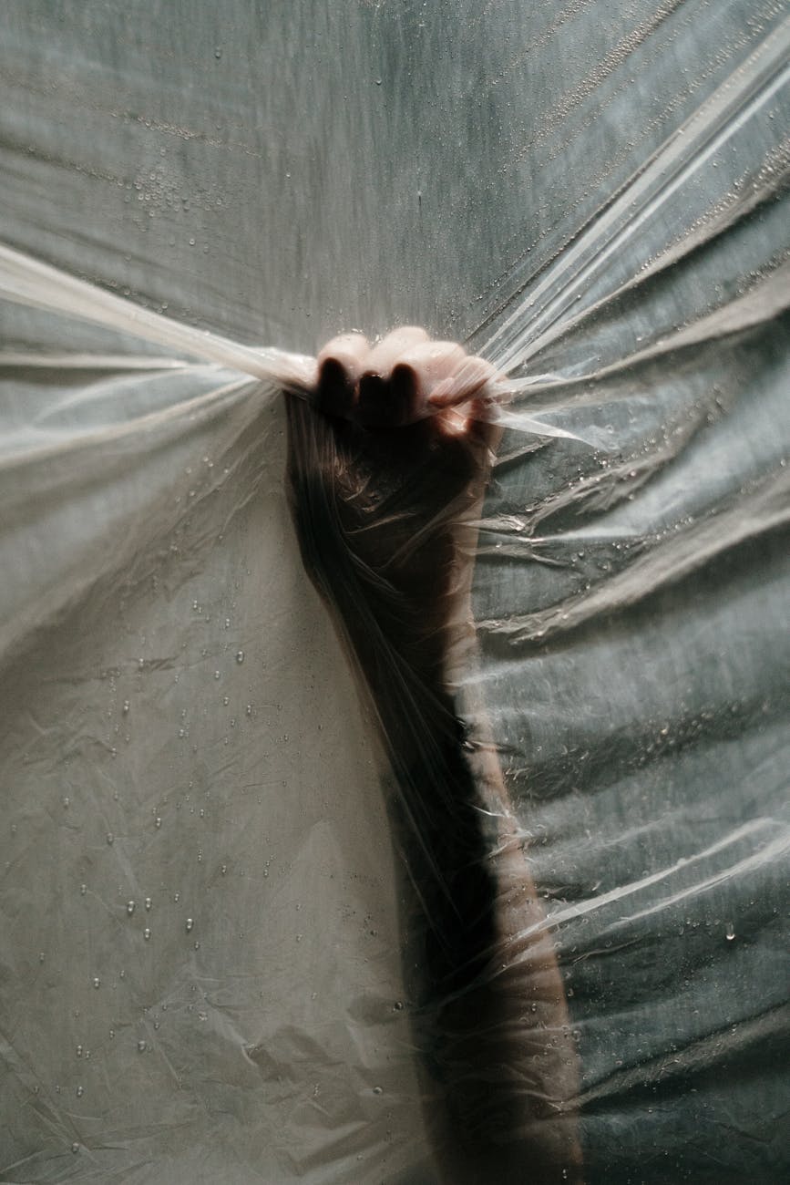 A hand gripping tight onto plastic, creating a thought-provoking conceptual image with water droplets.