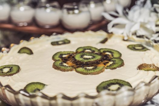Close-up of a kiwi and passionfruit cream tart, topped with fresh fruit slices, indoors.