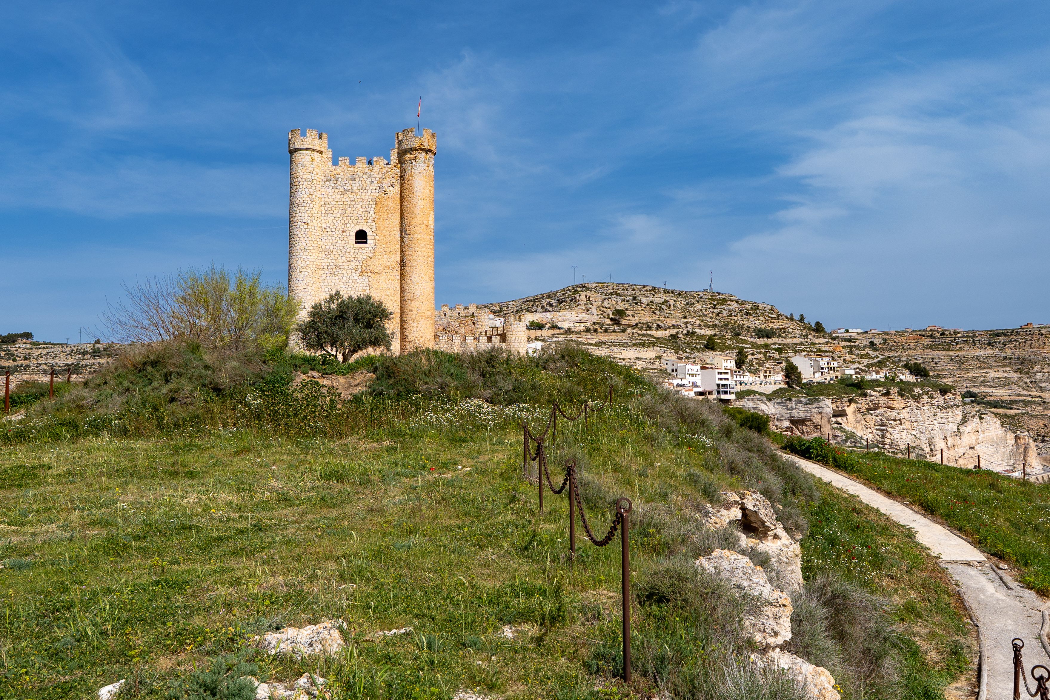 Scenic view of a medieval castle tower amidst lush greenery in Alcalá del Júcar, Spain.