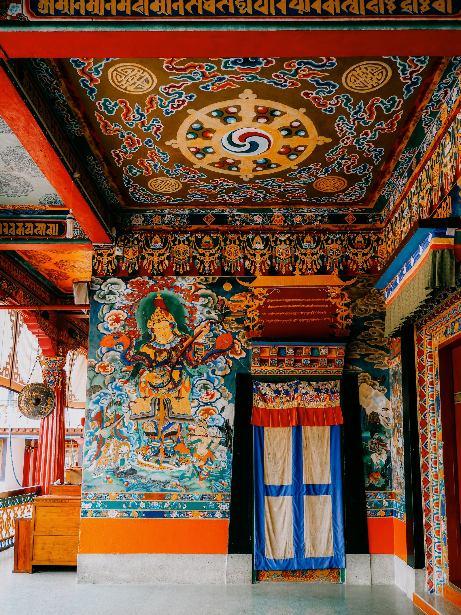 The painted porch of Rumtek Monastery, a lute playing guardian king on the wall and a mandala on the ceiling above