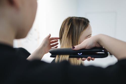 Foto De Enfoque Selectivo De La Persona Que Plancha El Cabello De Una Mujer