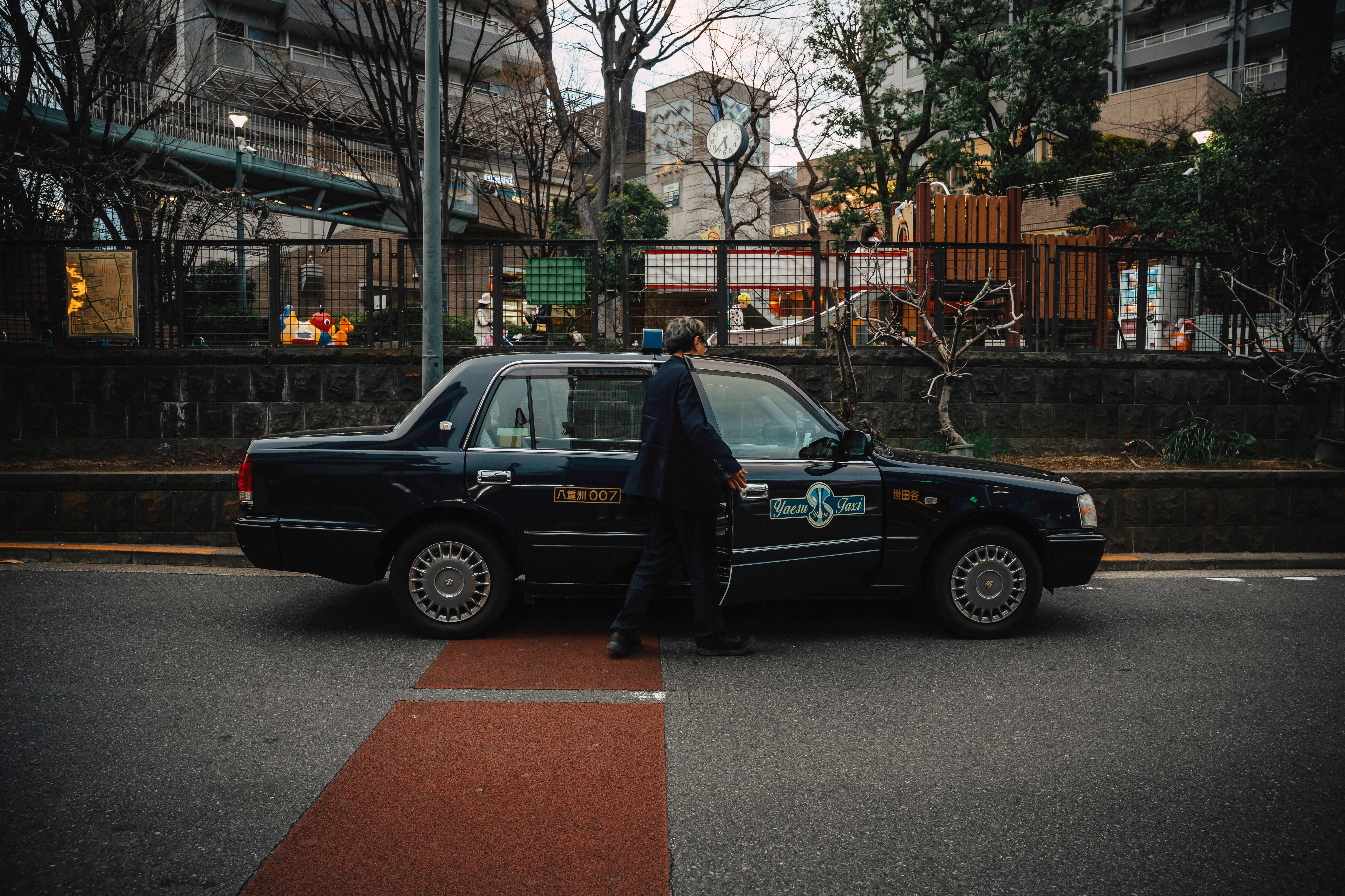 Man stepping into a taxi on a tree-lined city street with buildings behind.