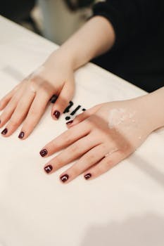 Close-up of manicured hands with burgundy nails in a beauty salon, showcasing skincare treatment.