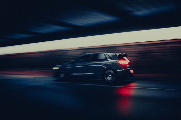 Dark hatchback moving through a lit underpass, background blurred by speed. Photo by Benni Fish on Pexels