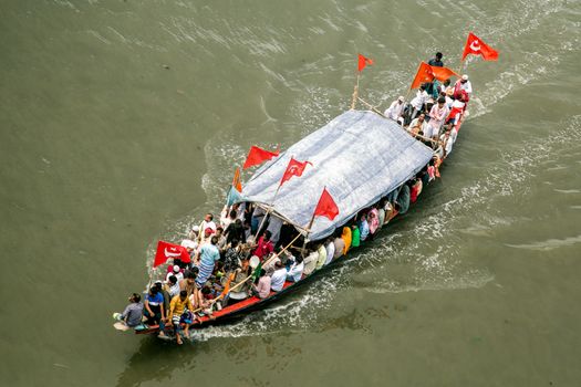 Aerial shot of a crowded boat with red flags navigating on a river, showing daily commute.
