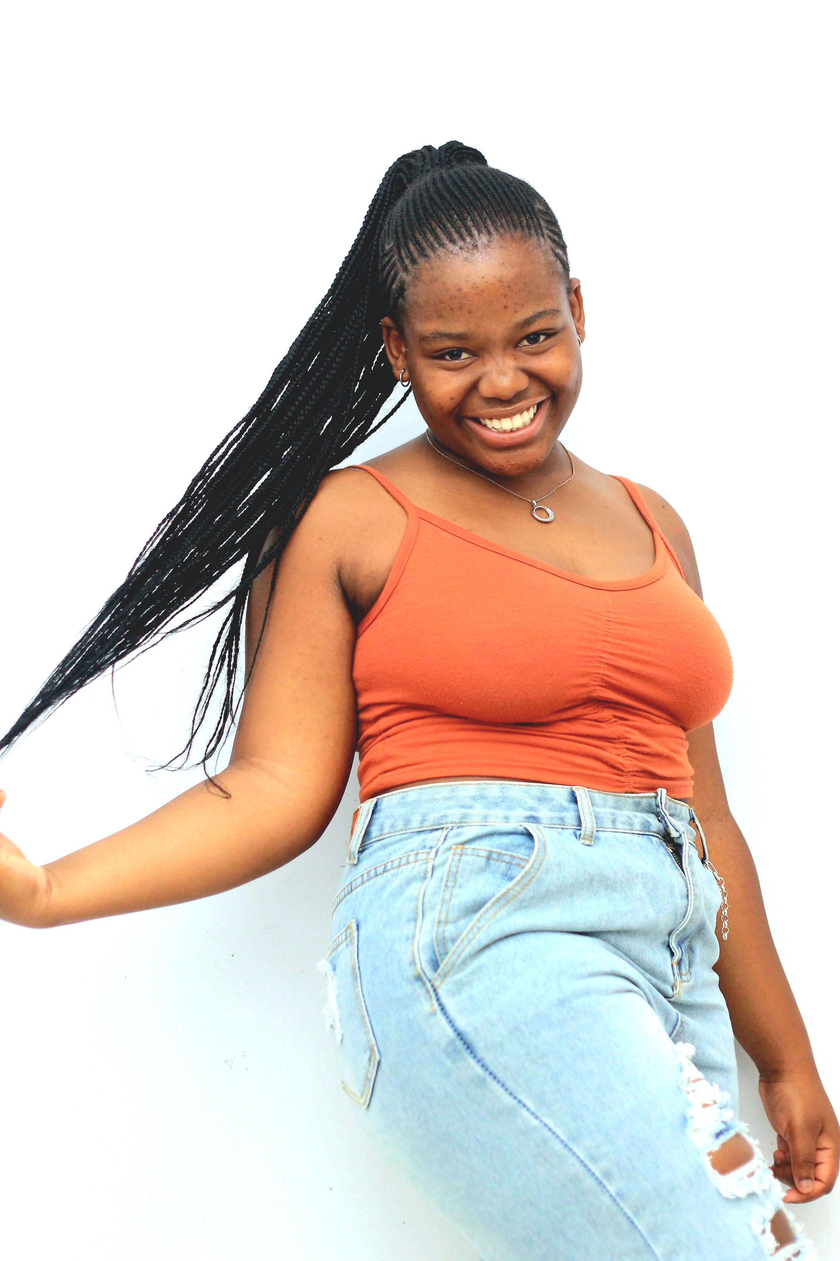 A cheerful young woman with braided hair posing against a white background, exuding confidence and style.