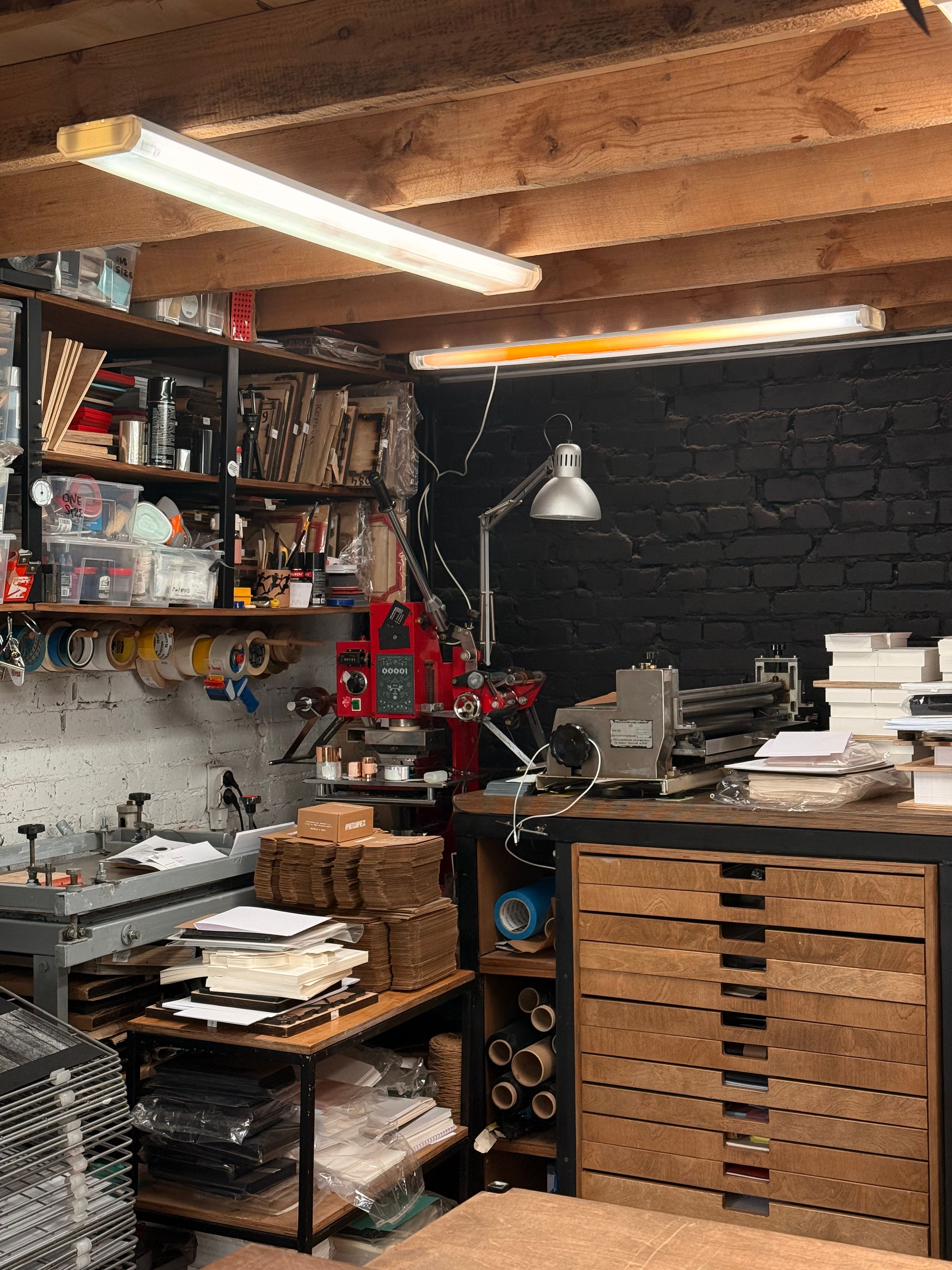 Atelier avec une presse rouge, une lampe d'établi articulée et des étagères chargées