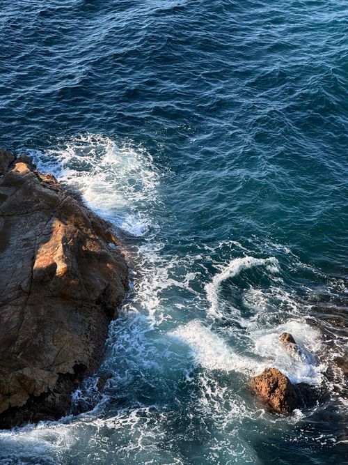 Free Waves crash on rocky cliffs under a clear sky, showcasing the ocean's raw power and natural beauty. Stock Photo