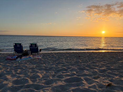 Two chairs on a sandy beach facing a serene ocean sunset, perfect for relaxation.