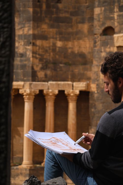 Free Artist sketching ancient columns outdoors. Captures creative process in a historical setting. Stock Photo