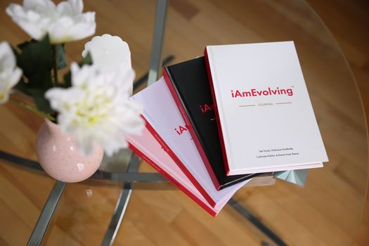 An elegant journaling scene featuring iAmEvolving books and white flowers on a glass table, ideal for self-care.