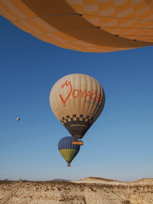 Free Colorful hot air balloons flying over the landscape of Cappadocia under a clear blue sky. Stock Photo