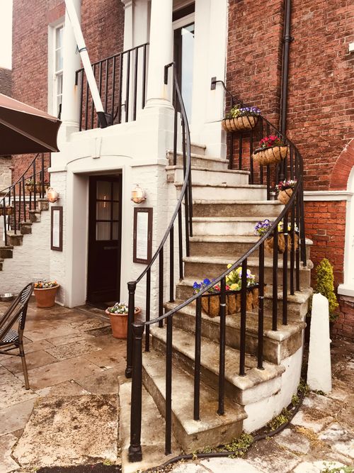 Free A charming restaurant entrance featuring a curved staircase adorned with vibrant flower pots. Stock Photo