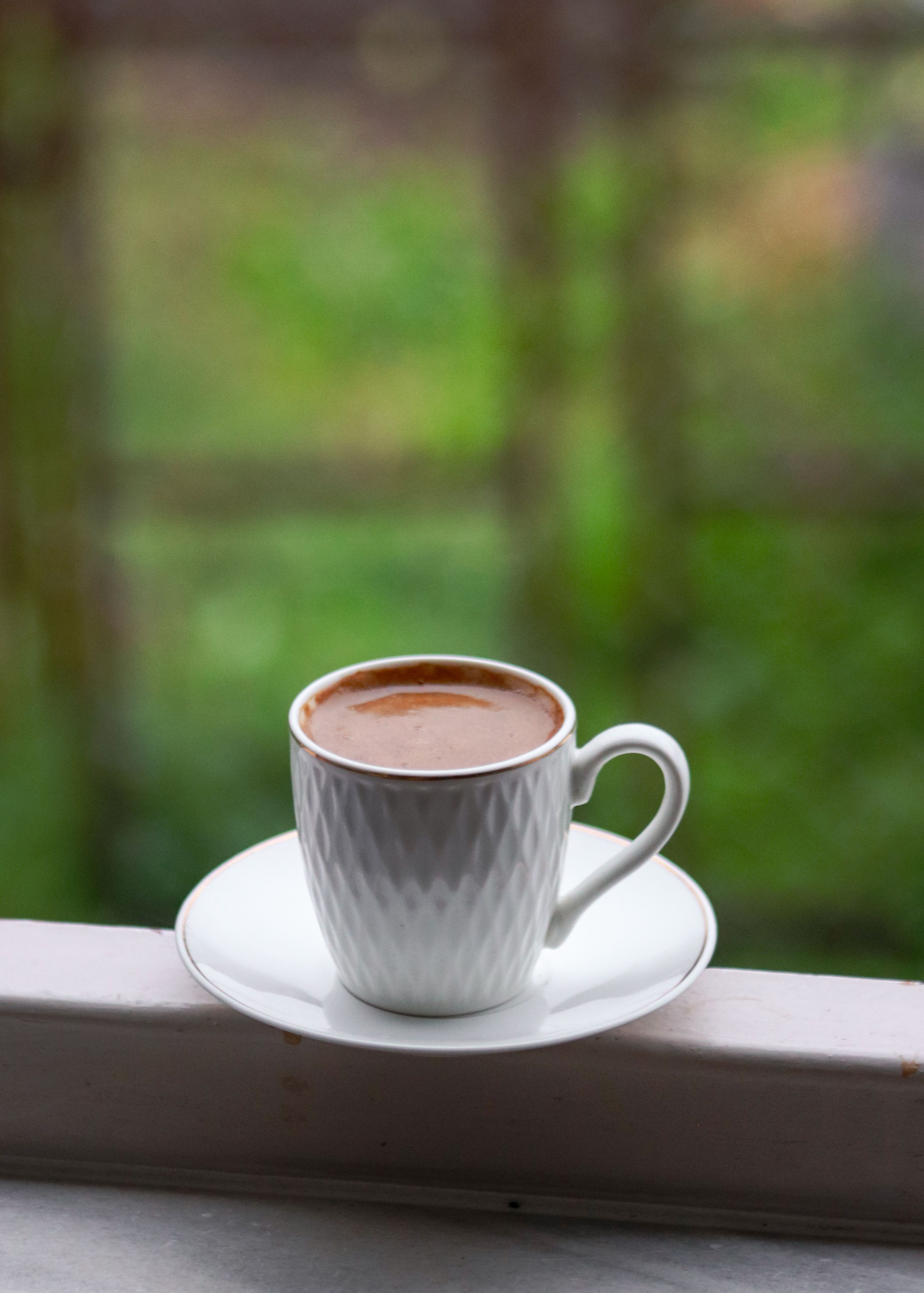Free A white coffee cup sits elegantly on a windowsill with a blurred green background. Stock Photo