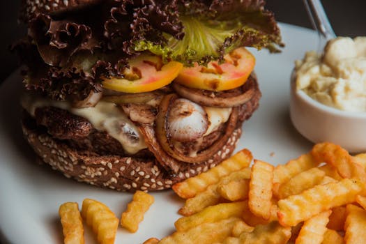 Close-up of a juicy cheeseburger with fries and a side salad on a plate.